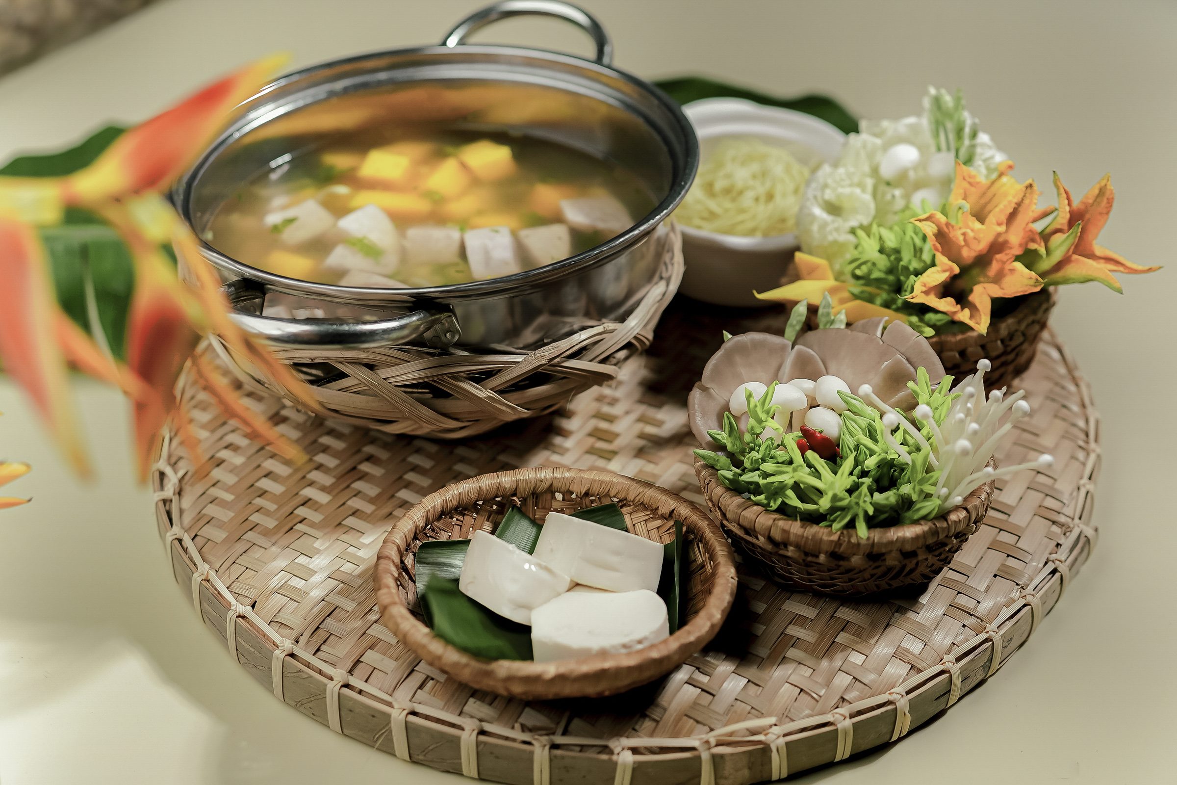 Mâm nguyên liệu lẩu bày trên mẹt tre — rau, nấm và đậu hũ tươi