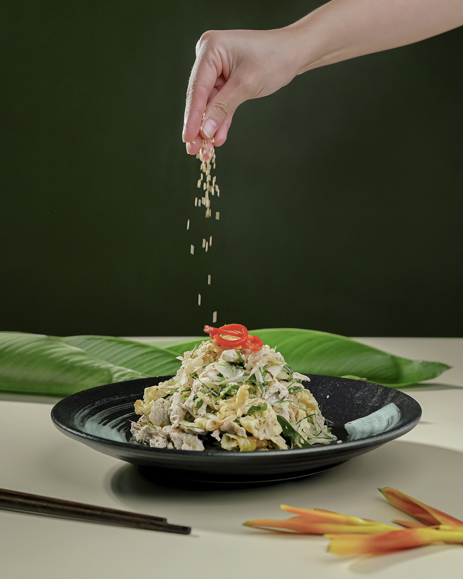 Bàn tay rắc mè lên dĩa gỏi trên nền xanh rêu