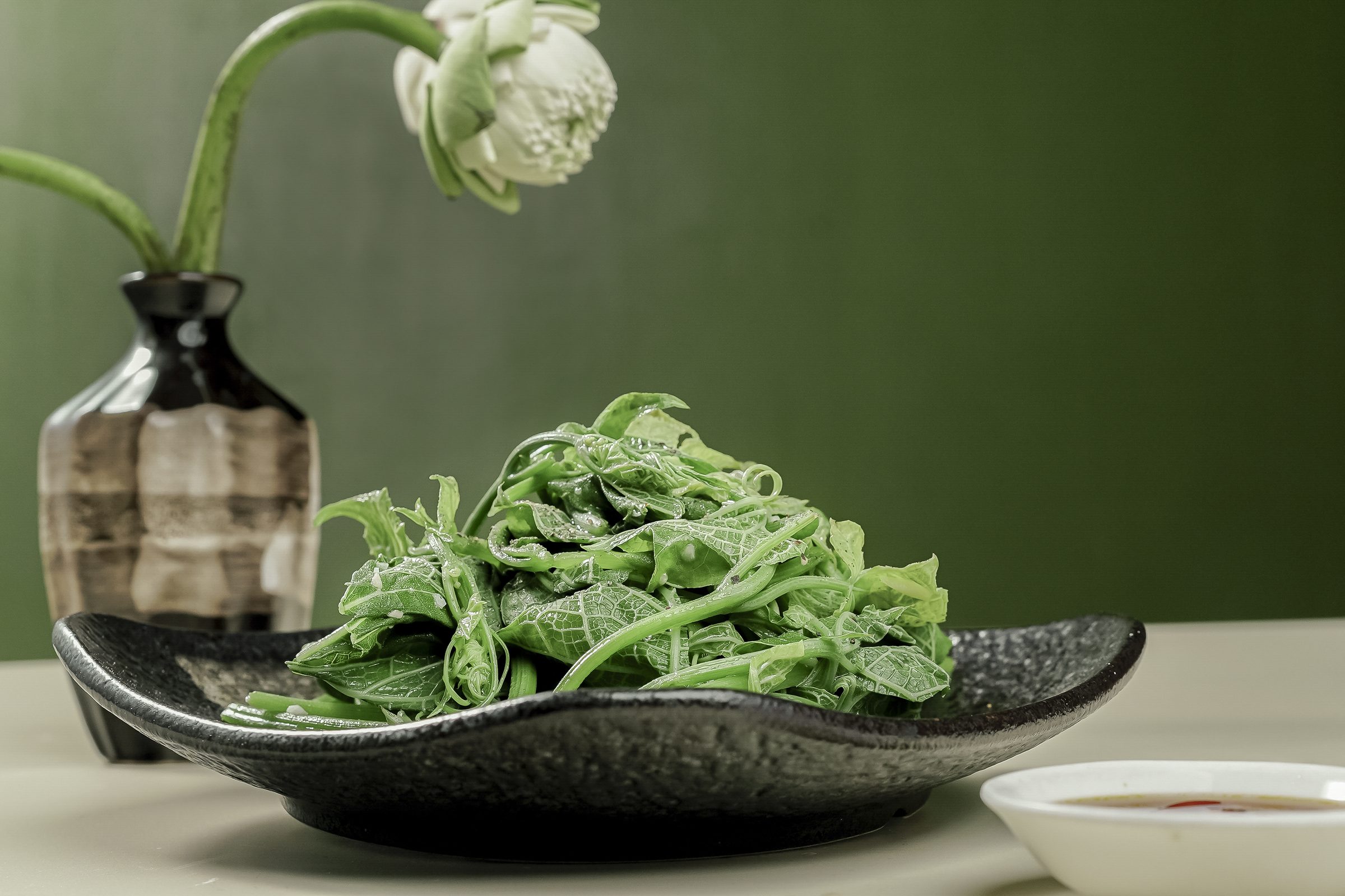 Dĩa rau xanh xào tỏi bên bình sen trắng